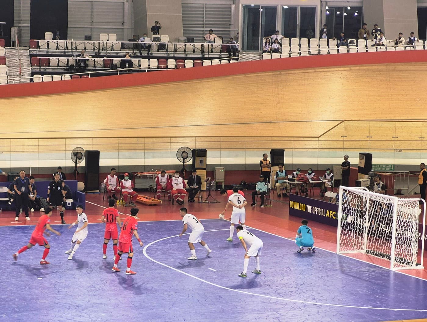 A futsal match on an indoor court, players chasing the ball near the goal.